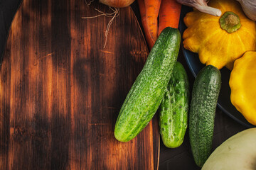 Fresh vegetables on a table with a cutting wooden board. Cucumbers, pumpkins and carrots on the table. A place to copy the space.
