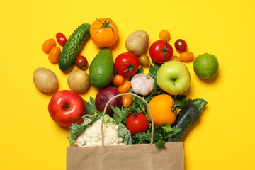 Delivery of vegetarian products. Paper bag with different vegetables and fruits on yellow background, top view