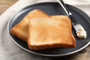 Delicious toasted bread slices with cream cheese and knife on table, closeup