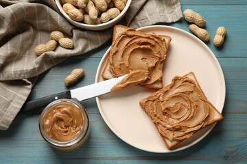 Tasty sandwiches with peanut butter and nuts on light blue wooden table, flat lay