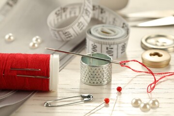 Different sewing tools on white wooden table, closeup