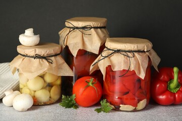 Different pickled products in jars and fresh ingredients on grey table