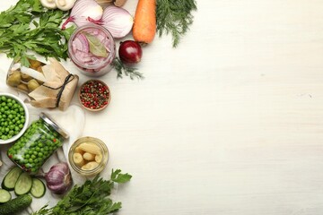 Different pickled products in jars and fresh ingredients on white wooden table, flat lay. Space for text