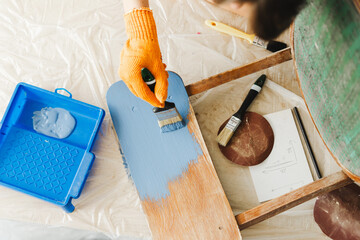 Craftsperson applying blue paint on wooden chair during renovation project