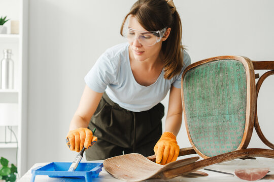 Woman restoring old chair using paint and varnish remover
