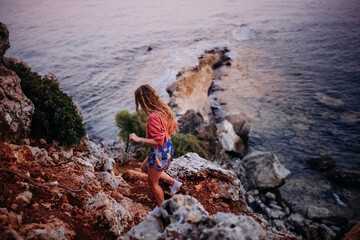Woman exploring rocky coastline during sunset near calm ocean waters