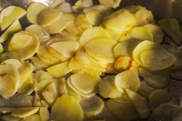 Thinly sliced potatoes are fried in a pan until golden brown. Background with the texture of narzan potatoes.