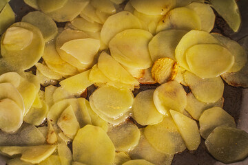 Thinly sliced potatoes are fried in a pan until golden brown. Background with the texture of narzan potatoes.