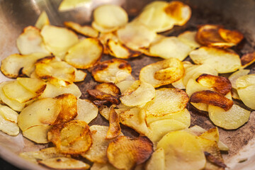 Potatoes fried in a pan until golden brown. Fried potato slices in a steel pan. Quick homemade vegetarian dish