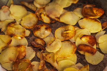 Potatoes fried in a pan until golden brown. Fried potato slices in a steel pan. Quick homemade vegetarian dish