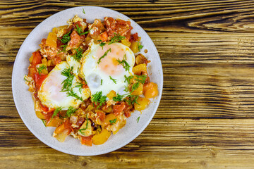 Homemade breakfast shakshuka with fried eggs, onion, bell pepper, tomatoes and dill on a wooden table. Jewish cuisine. Top view