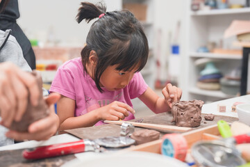 Young girl deeply engrossed in shaping clay during an art project. Her intense creativity are evident as she carefully molds the clay, showcasing the joy of hands-on learning and artistic expression.