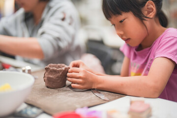 Young girl deeply engrossed in shaping clay during an art project. Her intense creativity are...