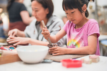 Young girl deeply engrossed in shaping clay during an art project. Her intense creativity are...
