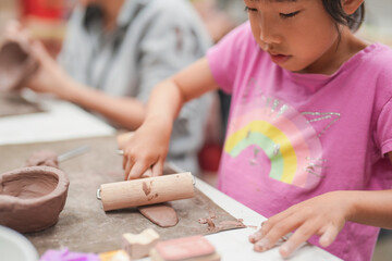 Young girl uses a rolling pin to flatten clay during an art class, Her engagement in the creative process highlights the joy and concentration involved in hands-on learning activities.
