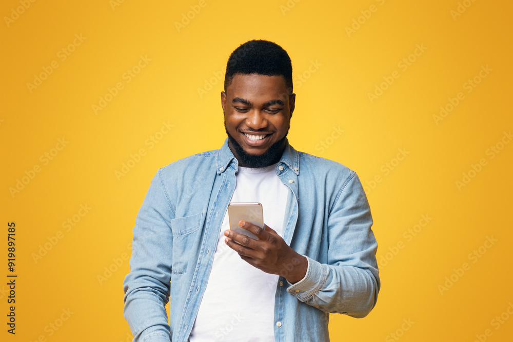 Poster Smiling african american guy reading message on smartphone over yellow studio background with copy space