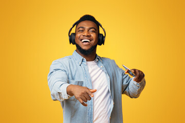 Portrait of handsome african guy in modern headphones enjoying listening his favorite music on smartphone