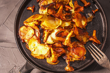 Fried potatoes with mushrooms Chanterelles in a black cast-iron frying pan with a fork on a gray background