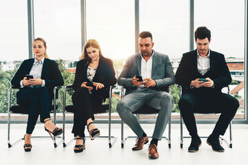 Businesswomen and businessmen using mobile phone while waiting on chairs in office for job interview. Corporate business and human resources concept. uds