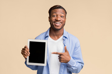 Smiling Afro Man Pointing Finger At Blank Tablet Computer Screen Standing On Yellow Background In Studio. Mockup