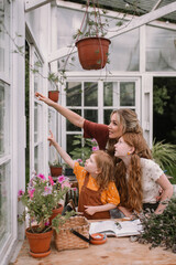 Woman mother and two red daughters girls care in greenhouse, do gardening in spring for Earth Day, look out the window, pointing hand gesture.