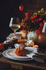 Elegant seasonal fall table setting with floral composition in a pumpkin vase as a centrepiece. White wine, burning candles, romantic cozy atmosphere of family dinner, private autumn wedding