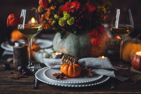 Beautiful elegant table setting for candlelight Thanksgiving Day dinner or Halloween party at home. Fancy dishware, porcelain plates. Floral centrepiece, pumpkins and burning candles as decor