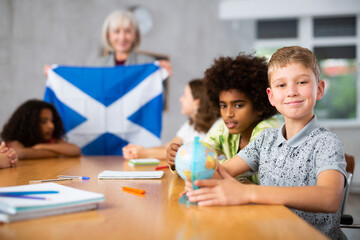 Fototapeta premium Ten-year-old schoolboy is studying the history of Scotland in lesson and is looking for her on the globe