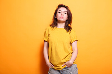 Portrait of cheerful person posing with confidence, holding hands in jeans pockets. Caucasian woman feeling positive and standing over orange background, looking at camera. Confident adult.