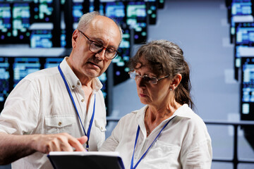 Fototapeta premium Old coworkers monitoring data center clusters, optimizing them for data processing requirements of AI applications. Skilled admins working in server room used for machine learning