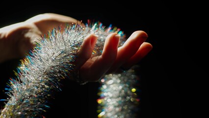 New Year's tinsel in a woman's hand on a black background