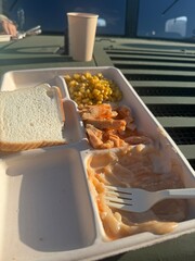 Lunch tray with pasta, corn, and bread on a table in a sunny outdoor setting