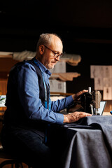 Senior tailor meticulously cutting fabric material with professional sewing machine in atelier shop...