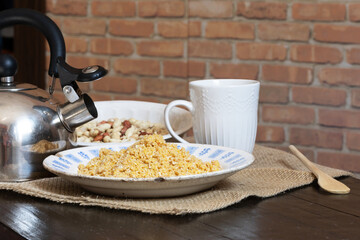 Homemade peanut brittle, a type of farofa, in an old plate with signs of age, next to a kettle and on top of a rustic tablecloth