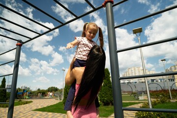 Mother lifts her daughter in a sunny playground on a summer afternoon