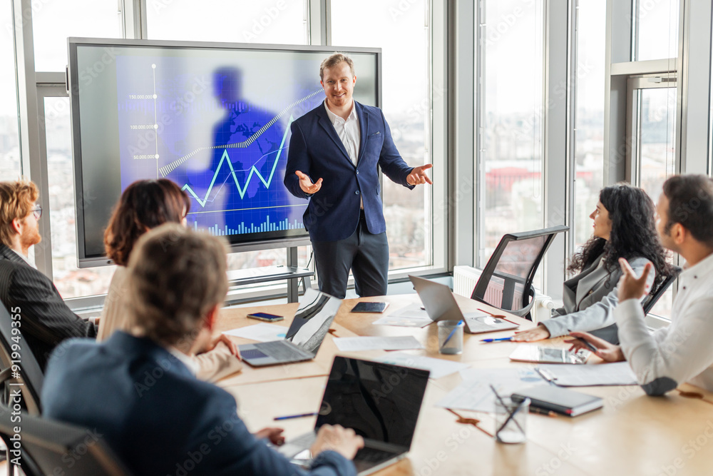 Fototapete a businessman stands in front of a large screen displaying a financial chart, pointing to the data a
