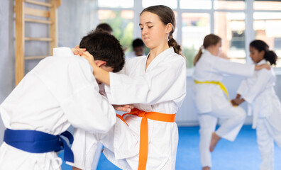 Confident determined teenage girl engaging training sparring during jiu-jitsu class, performing...