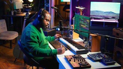 Talented famous composer writes down new verses and lyrics in home studio, composing music with digital software. Artist songwriter works with audio equipment and gear, recording tracks. Camera B.