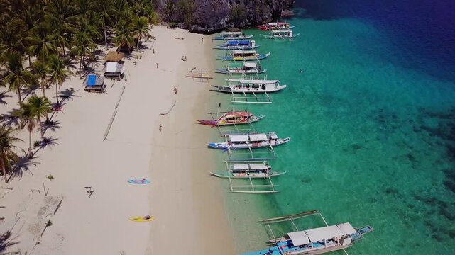 Aerial view of beautiful white sand beach, with palm trees and filipino boats in Siete Pecados Beach, Palawan, Philippines. 