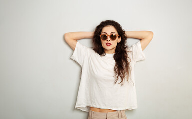 Naklejka premium Fun relax smiling woman posing in fashion sunglasses and white t-shirt on white wall background with empty copy space. Happy lifestyle