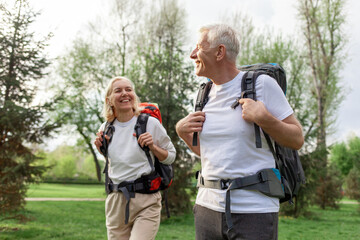 elderly athletic couple of seniors man and woman with hiking backpacks travel in the forest...