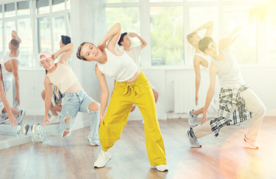 Positive teenage girl practicing hip hop backbend moves in training hall during group dancing classes - Powered by Adobe