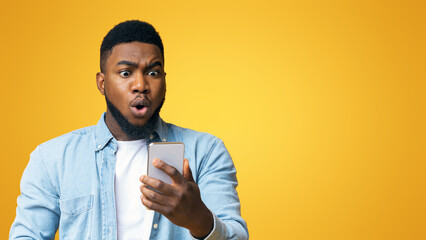 Unexpected message. Astonished african american man looking at smartphone screen in shock, standing...