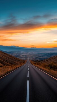 A winding road stretches towards a vibrant sunset over rolling hills, showcasing the beauty of nature and travel.