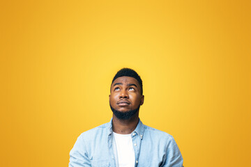 Doubtful african american man looking upwards at copy space on yellow background