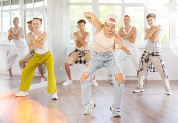 Fototapeta premium Plastic teenage girl engaged in hip-hop dance against background of others performing dance pose in row