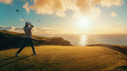 A man hits a golf ball down the hill towards the ocean.