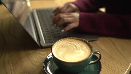 Close-up of a cup of coffee with a girl working on a laptop in a cafe in the background.