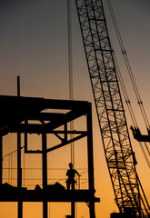 Detail vertical image of large construction crane and a iron beam frame in silhouette at sunset or...
