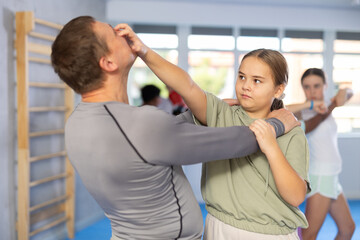 Determined tween girl attacking eyes of male coach during sparring as self-defense tactic during group session in training room..